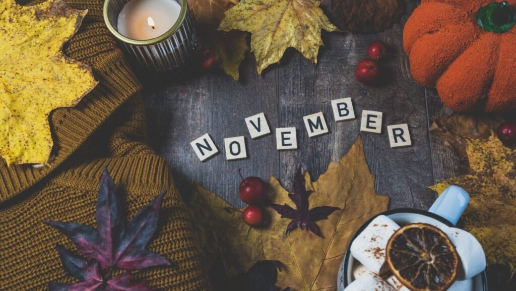 Warm autumn still life featuring a candle, pumpkin, leaves, and hot drink for November ambiance.