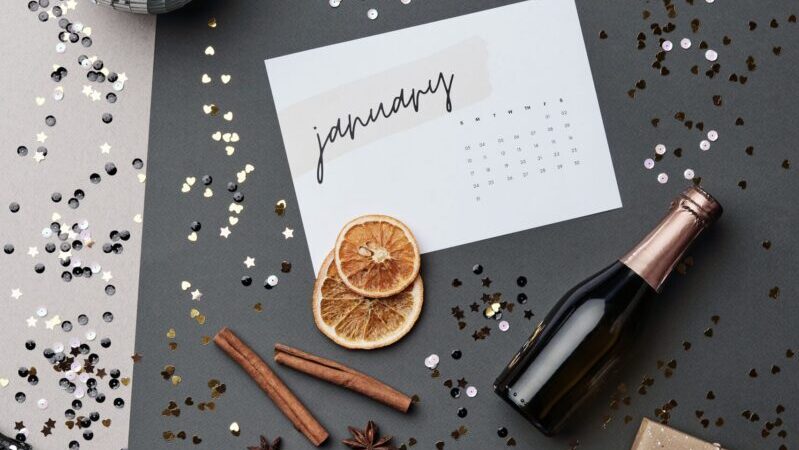 Stylish flat lay with New Year elements: calendar, bottle, gift, spices on a festive background.